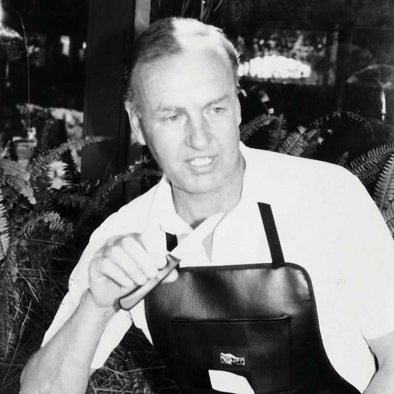Bernd Dressler of Messermeister wearing a black leather apron and holding a knife in his hand while talking. 