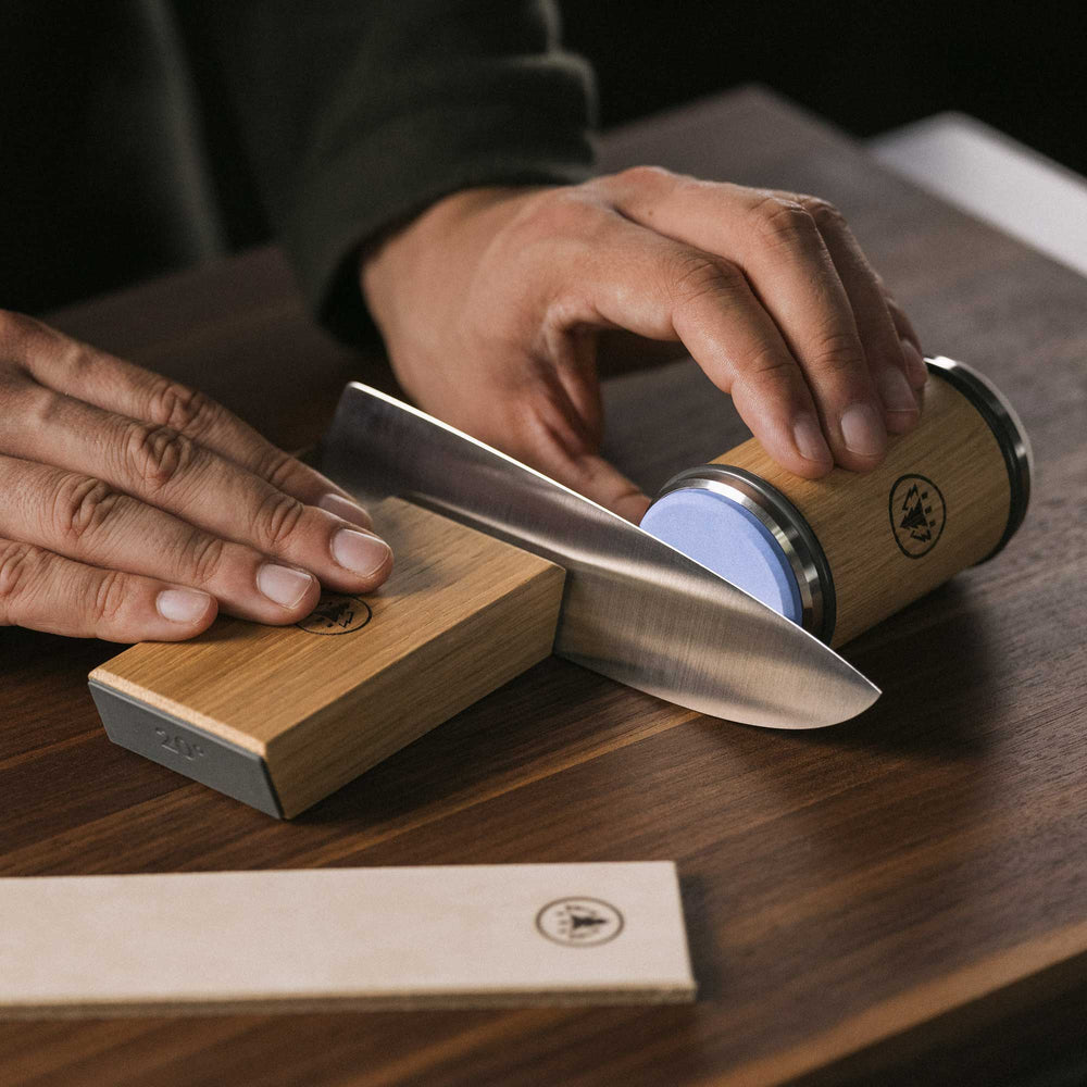 Person using Horl 3 Oak Sharpener Kit with Cylinder Sharpener and Angle Guide to sharpen a knife on a wooden surface.