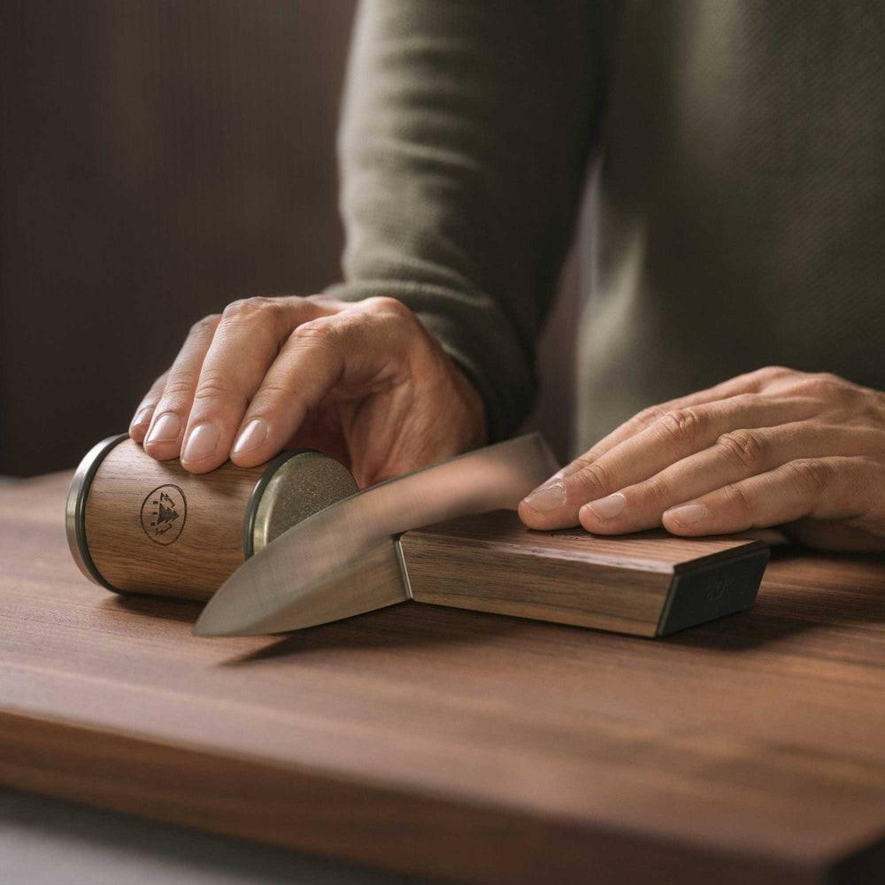 Person using Horl 3 Walnut Rolling Sharpener Kit with Cylinder Sharpener and Angle Guide to sharpen knife on a wooden surface