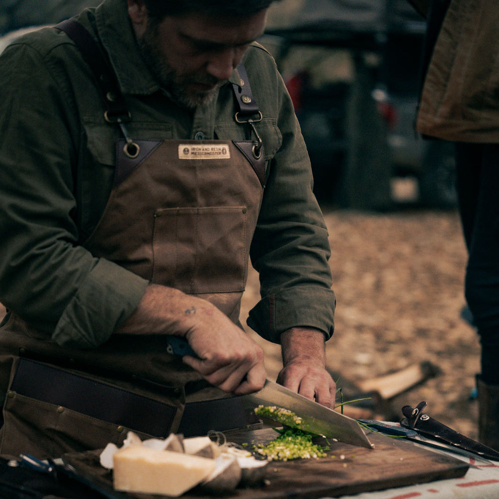 man wearing the brown leather apron while chopping veggies outdoors