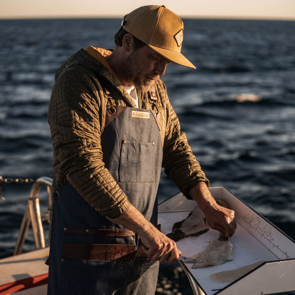man on a boat wearing the apron and fileting fish