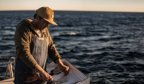 Chef Adam Glick on a boat at sea  filleting a fish with a Messermeister Overland Fillet Knife with a sunset background