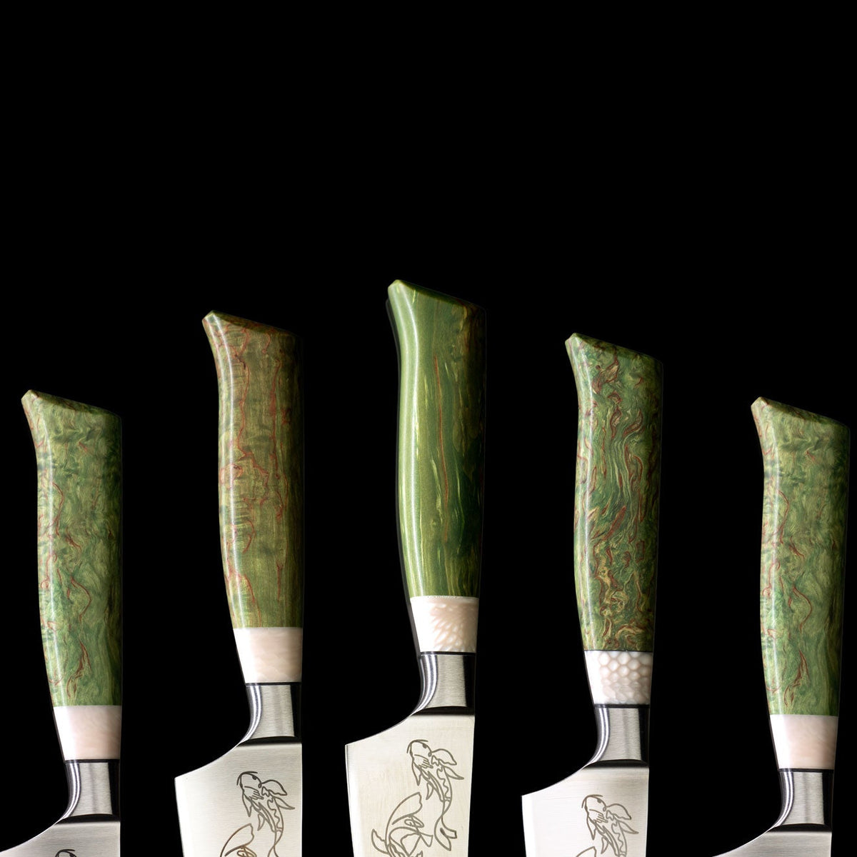 Five kitchen knives with green-dyed stabilized wood handles and engraved fish designs on the blades, arranged against a solid black background.