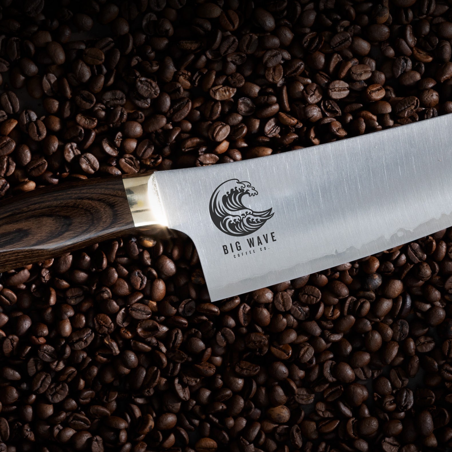 Wave logo engraving on a Kawashima Chefs knife with dark wood handle on top of coffee beans