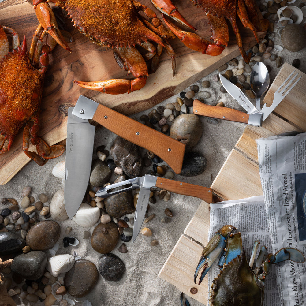 Crabs on a wooden board with Messermeister Adventure Chef knives and a newspaper on a pebble surface