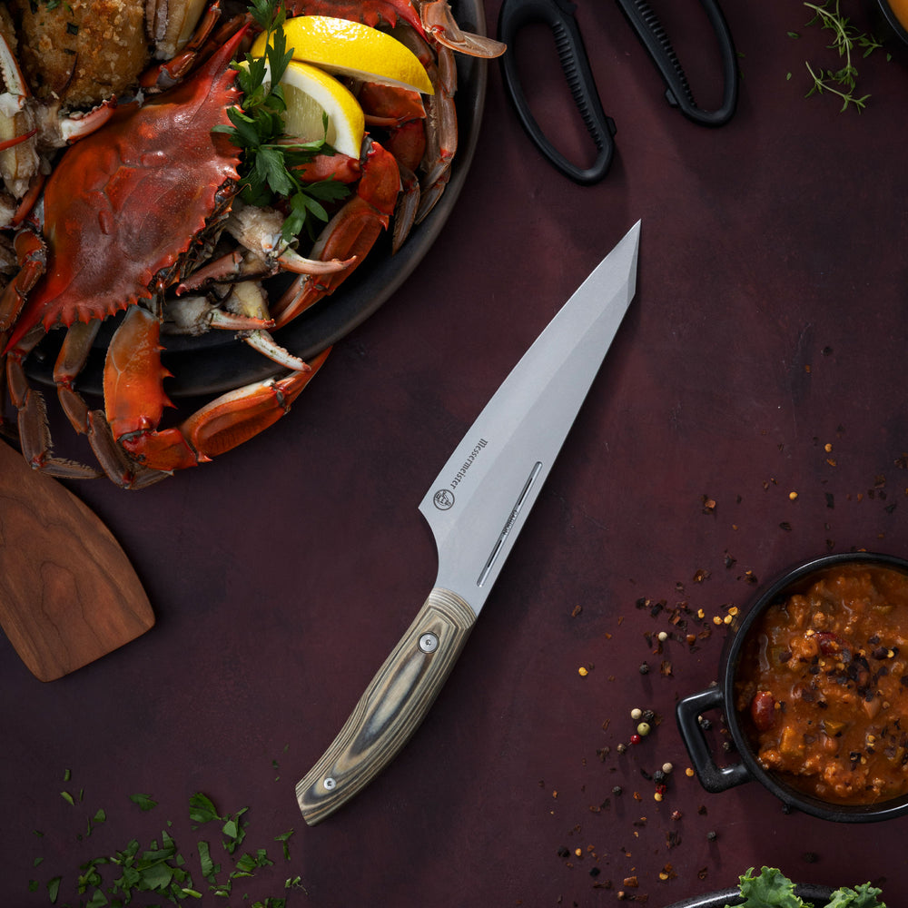 Messermeister Carbon April Bloomfield Chef Knife on a dark red surface with a crab, lemon, and other ingredients