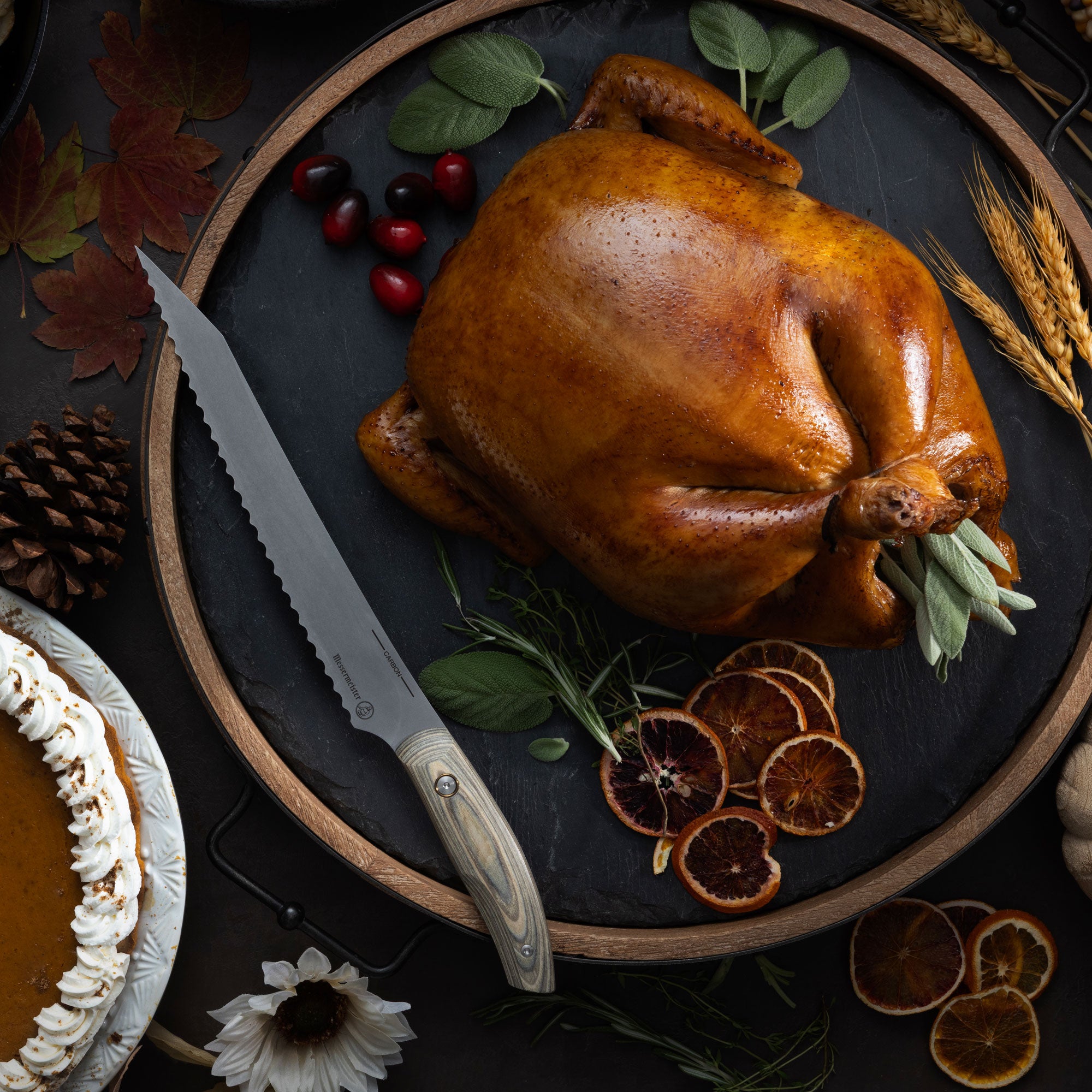 Roasted chicken on a dark plate with a Messermeister Carbon Scalloped Slicer, surrounded by autumn decorations.