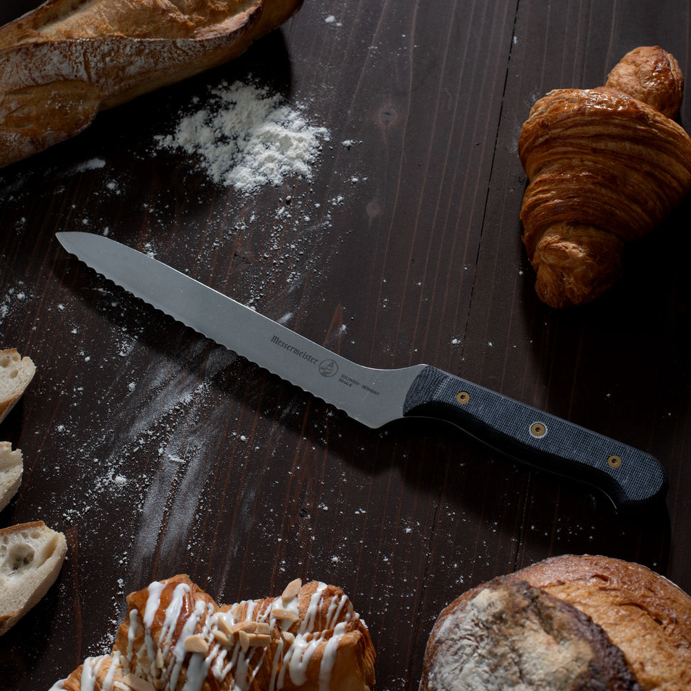 Messermeister Custom Offset Bread Knife on dark wood surface with Bread Items and flour