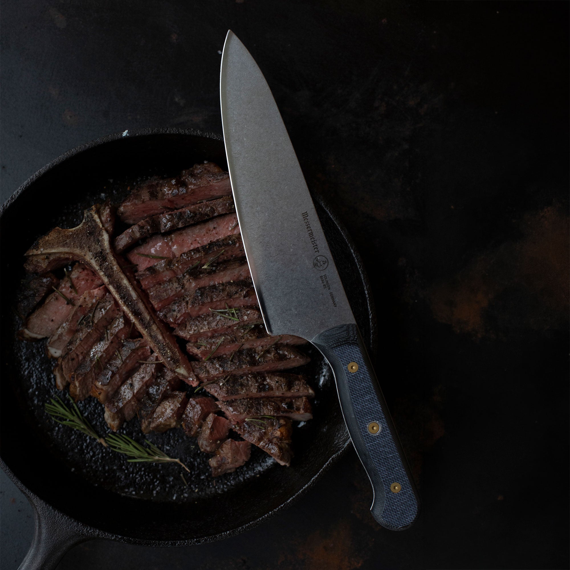 Messermeister Kawashima Custom Steak Knife with a steak in cast iron pan on a dark surface