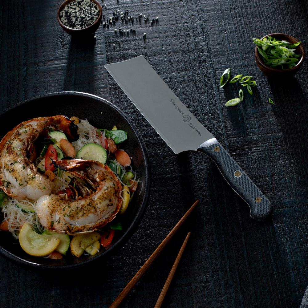Plated dish with seafood and vegetables, Messermeister Custom Nakiri knife, and chopsticks on a dark surface
