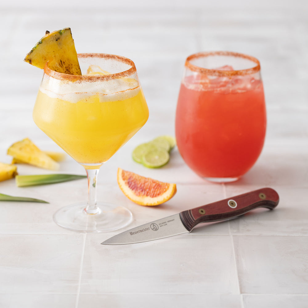 Two bright cocktail drinks on white surface background and fruit with Messermeister Custom Red Paring Knife