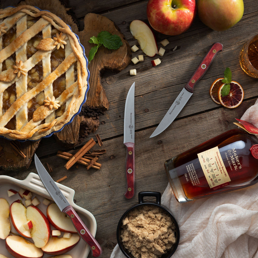 Messermeister Custom Red Steak Knives with apple pie, apples, cinnamon sticks and bourbon on a wooden surface