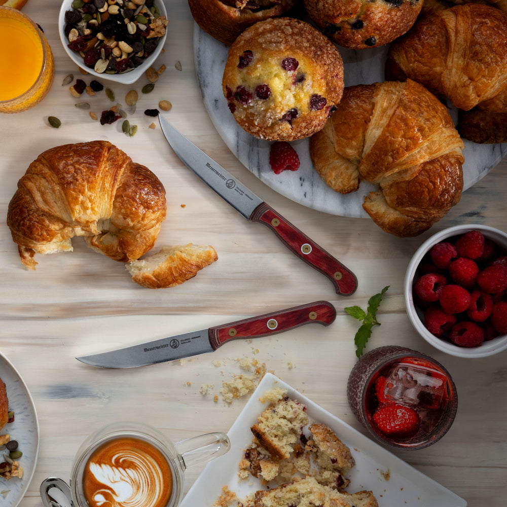 Messermeister Custom Red Steak Knives with cafe pastries, rasberries, orange juice, and a cappuccino on a light wood surface 