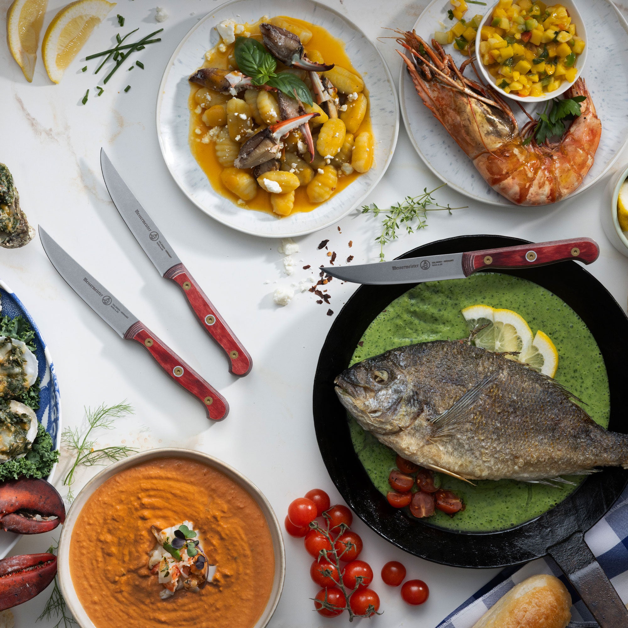 Messermeister Custom Red Steak Knives with Feast of Seven Fishes, hummus, tomatoes, and gnocchi on a white marble countertop