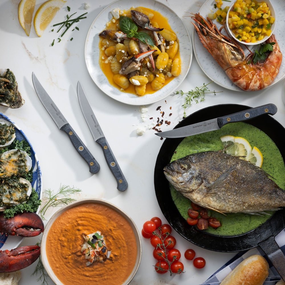 Messermeister Custom Steak Knives with a Feast of Seven Fishes, hummus, tomatoes, and gnocchi on a white marble countertop