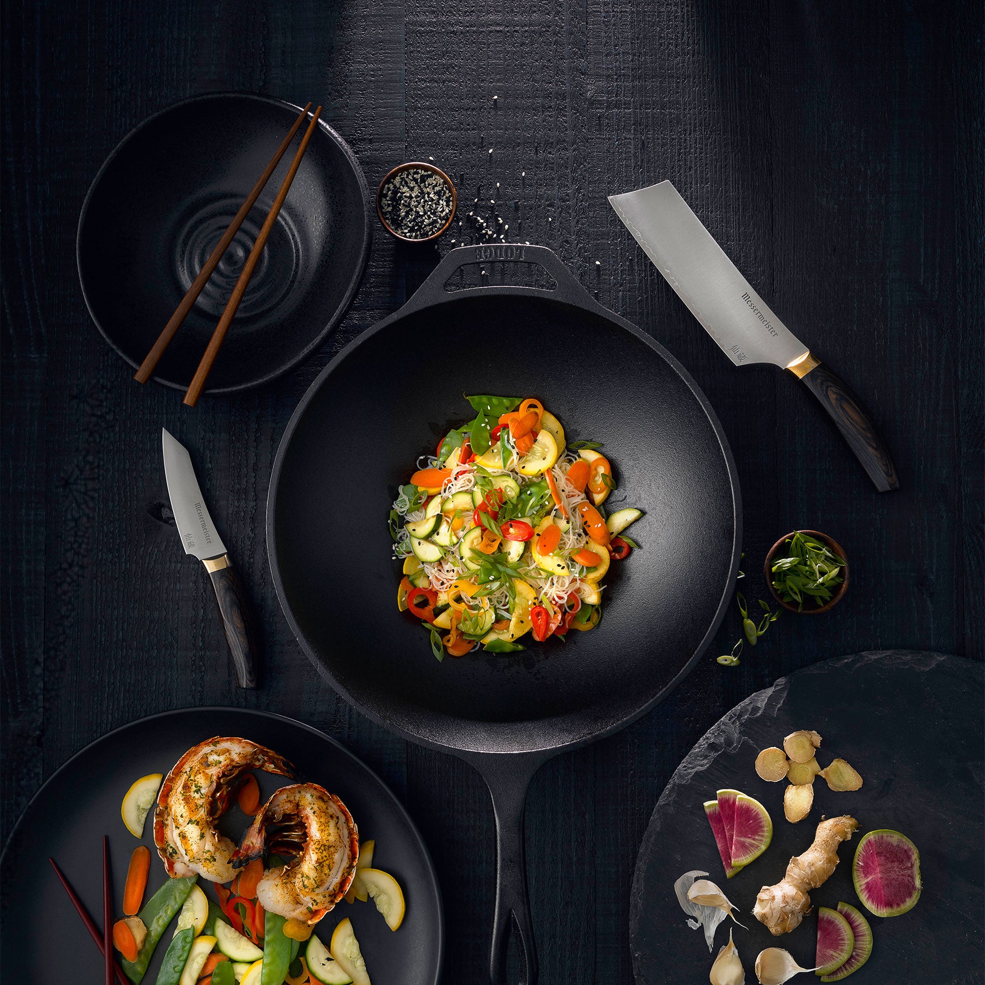 Messermeister Kawashima Nakiri and Paring Knife with stir fried noodles and vegetables in wok on a black color wood surface