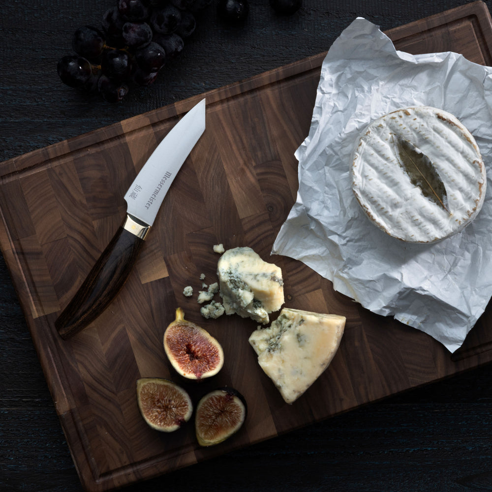 Messermeister Kawashima Paring Knife on cutting board with cheese, figs and grapes on a dark surface
