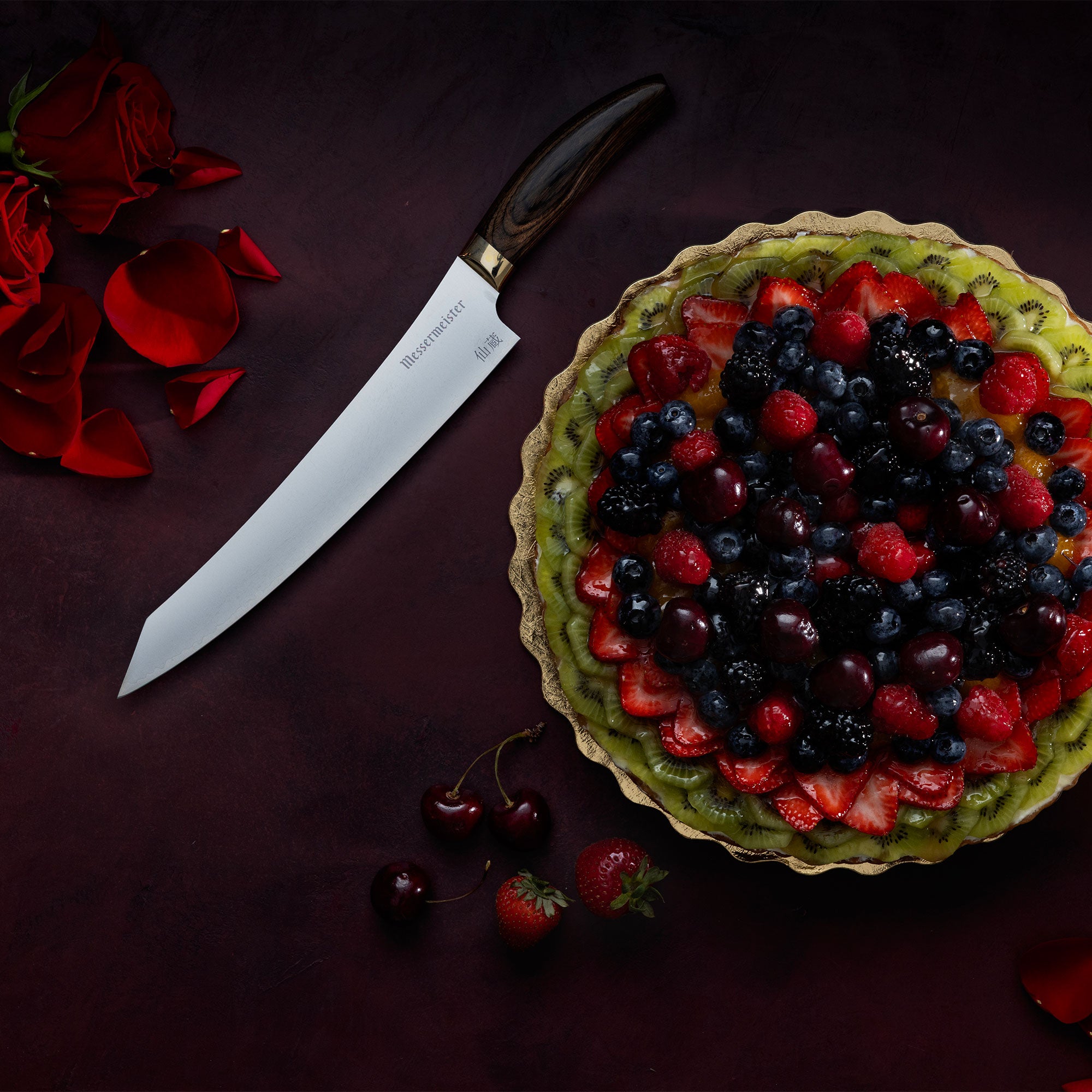 Messermeister Kawashima Slicing Knife with a fruit tart, cherries, strawberries and rose petals on a dark red surface