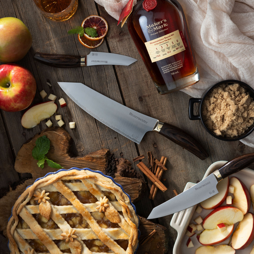 Messermeister Kawashima Starter Set of Chef Knife, Paring and Utility with apple pie, apples, cinnamon sticks and bourbon on a wooden surface