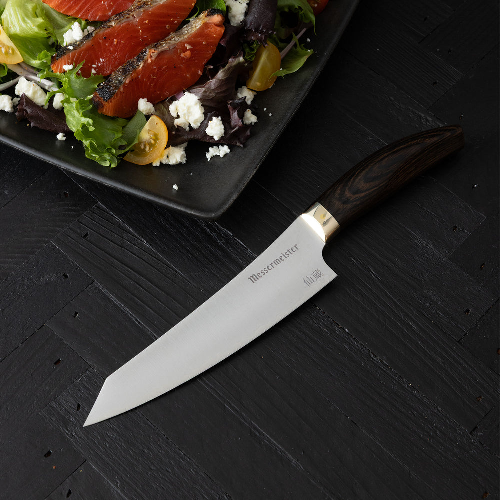 Messermeister Kawashima Utility on a black surface next to a plate of salad.
