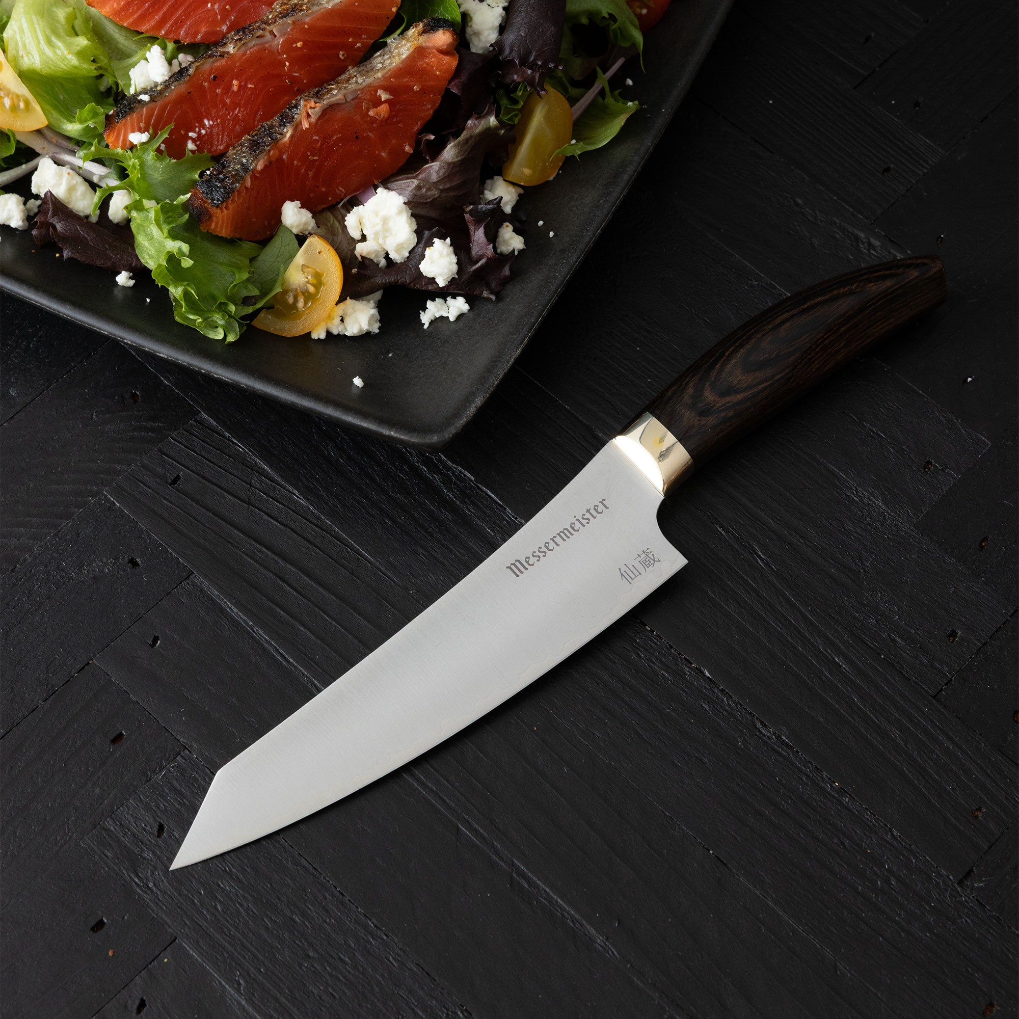 Messermeister Kawashima Utility on a black surface next to a plate of salad.