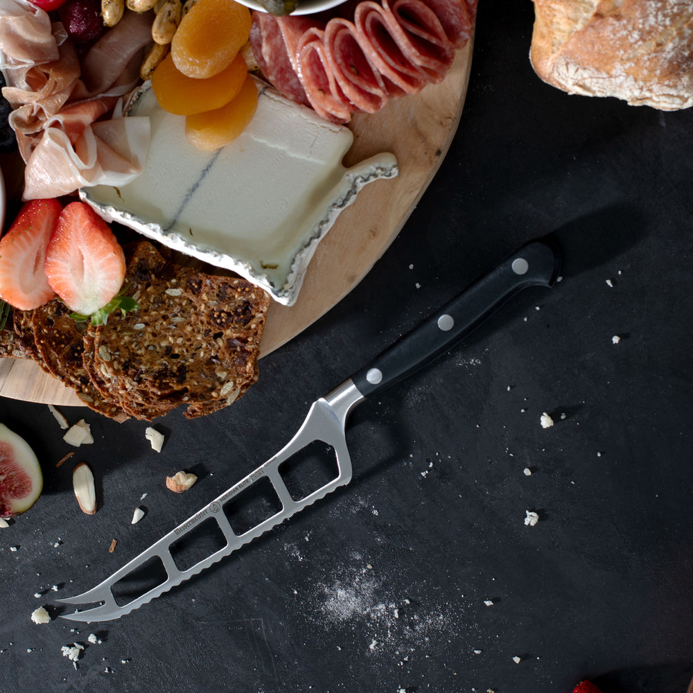 Messermeister Meridian Cheese and Tomato Knife on dark background with charcuterie spread with various meats, cheeses and fruit