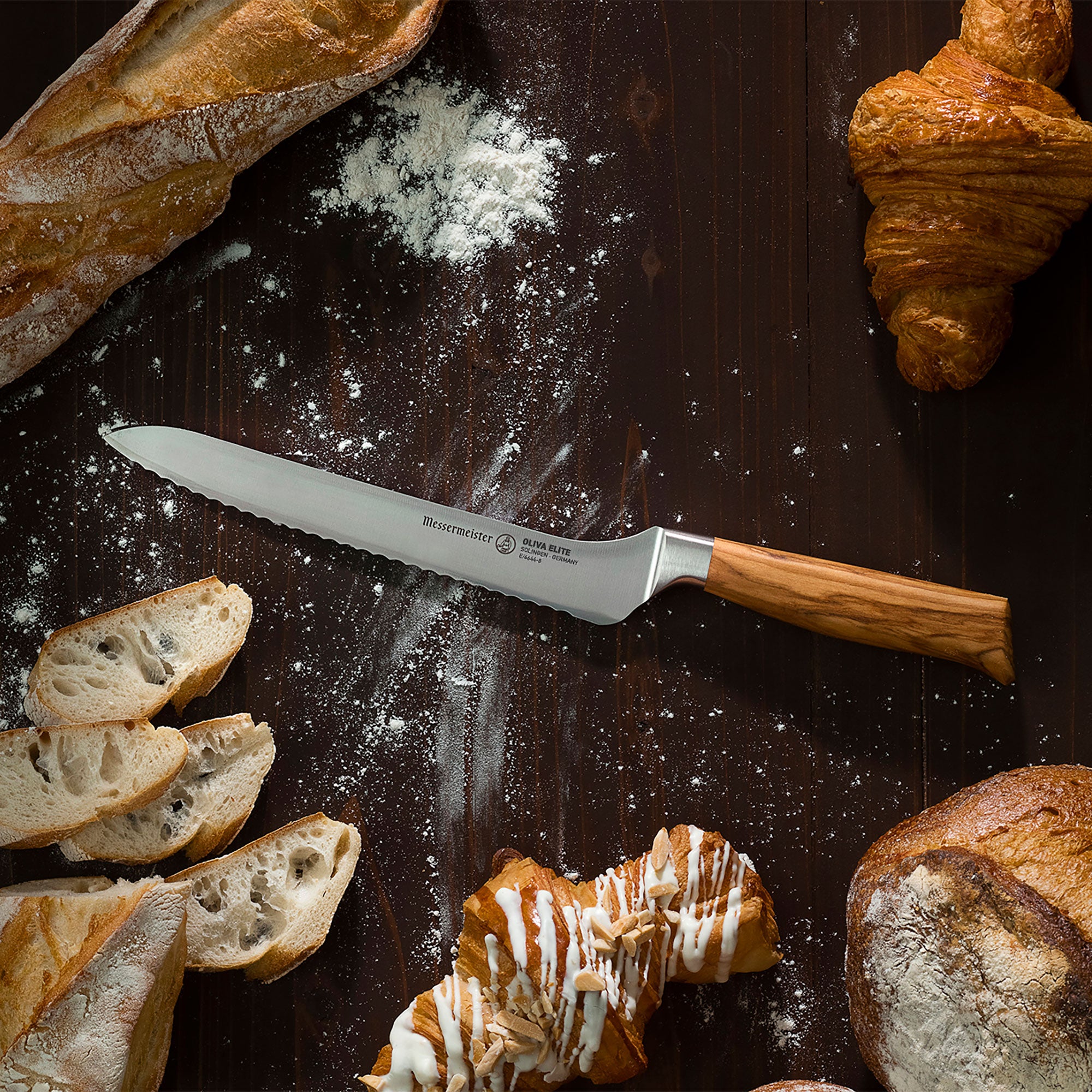 Messermeister Oliva Offset Bread Knife on a wooden surface with bread slices and pastries