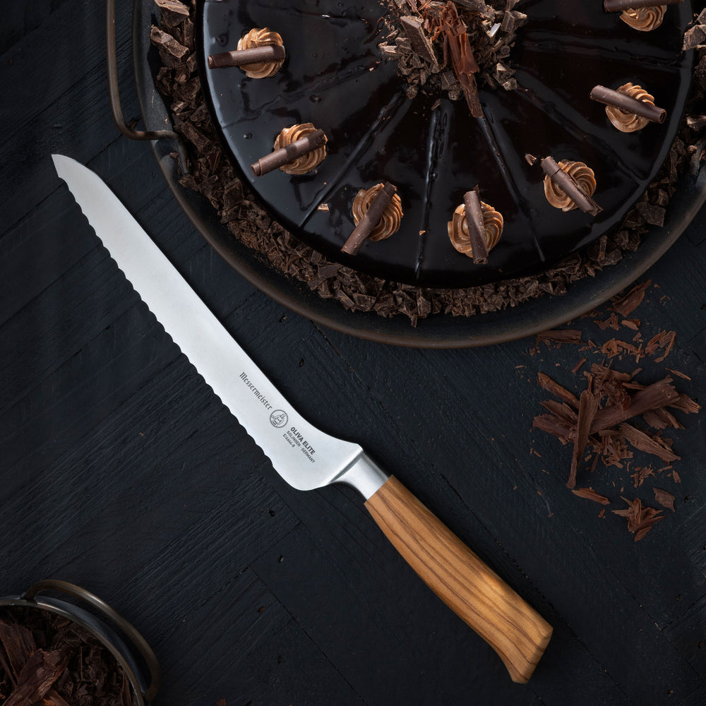 Messermeister Oliva Offset Bread Knife with wooden handle on a dark surface with chocolate elements
