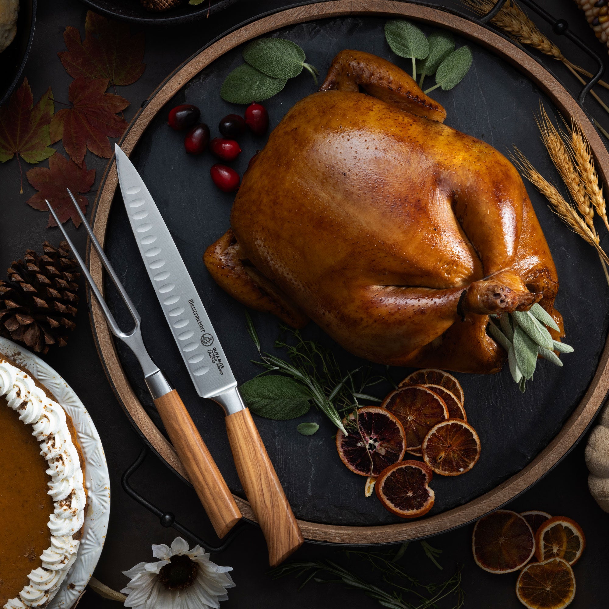 Roasted turkey on a dark surface with Messermeister Oliva Carving Set with Slicing Knife and Fork, pumpkins, and autumn leaves.