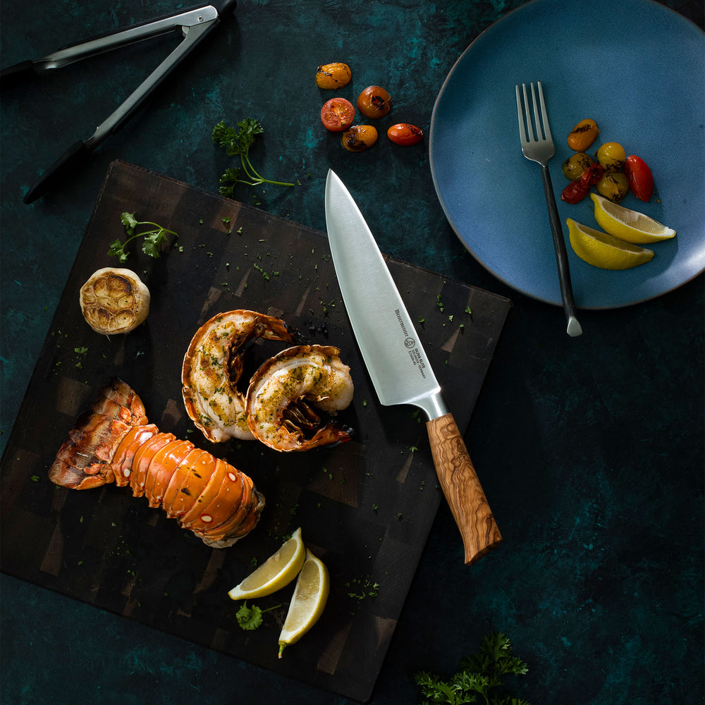 Garnished lobster seafood platter with a Messermeister Oliva Chef knife on a dark surface