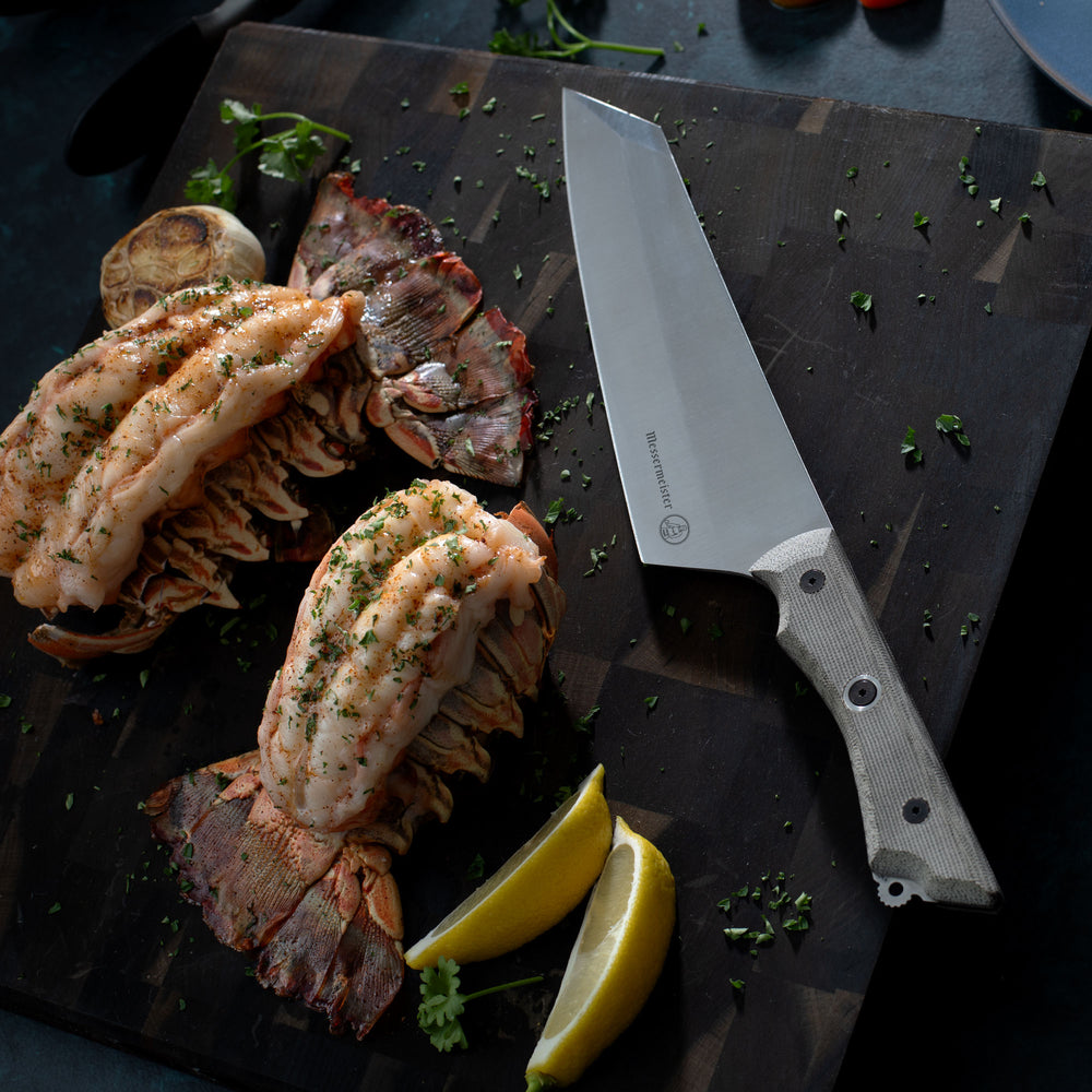 Steamed lobsters with lemon wedges and a knife on a dark wooden cutting board surface with Overland Chef Camp Knife