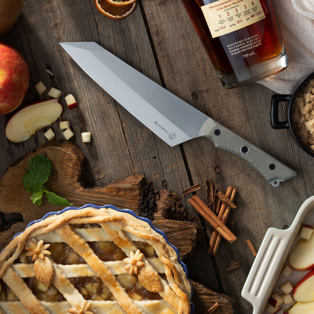 Messermeister Overland Chef Camp Knife on a wooden surface with an apple pie, apples, and cinnamon sticks.