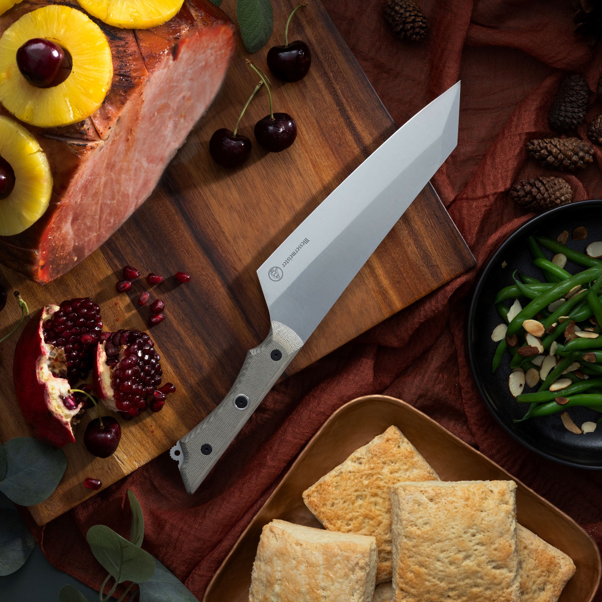 Wooden cutting board with a Messermeister Overland Chef Camp knife, sliced fruit, and snacks on a rustic background