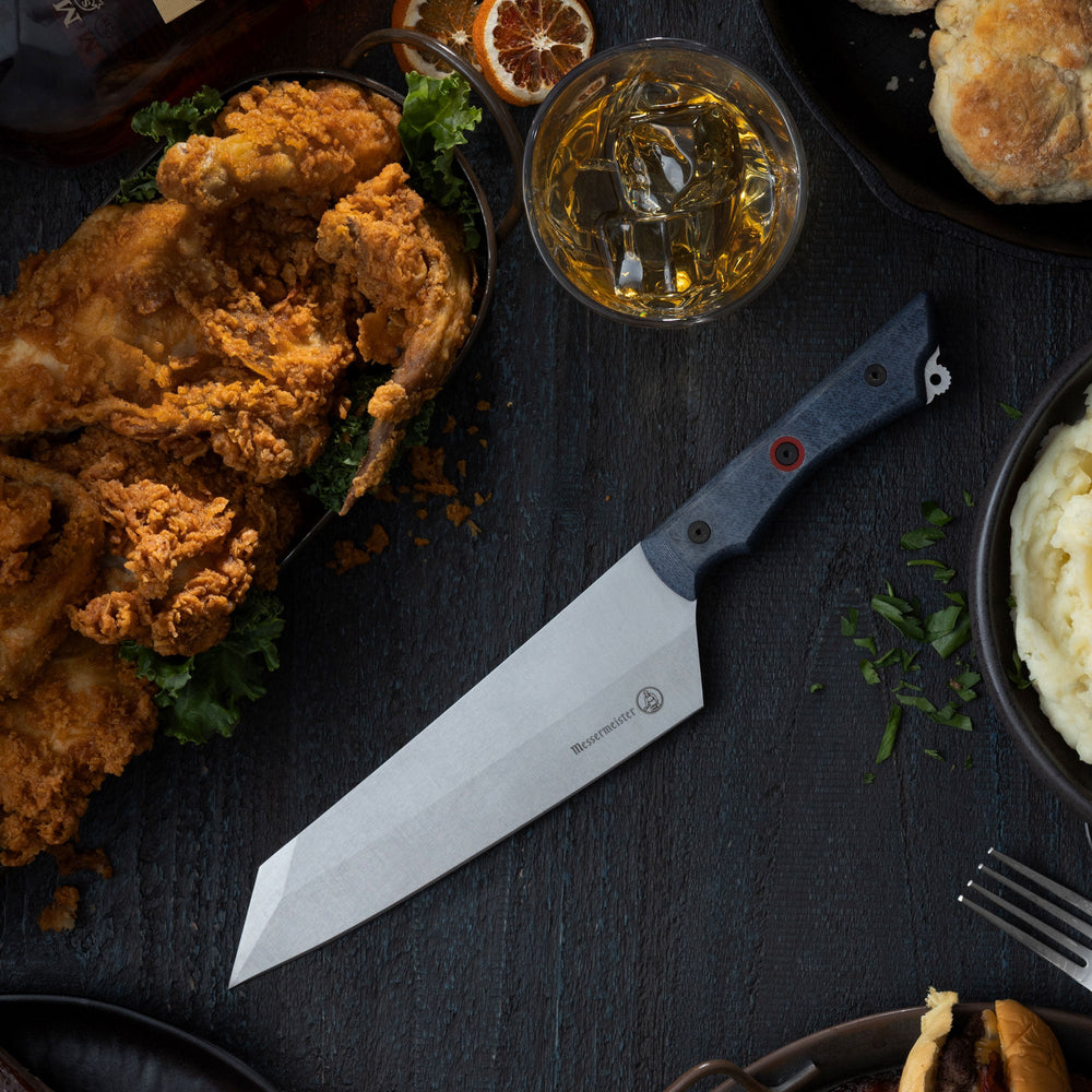 Fried chicken with a Messermeister Overland Field and Flame Camp knife and a glass of bourbon on a dark surface