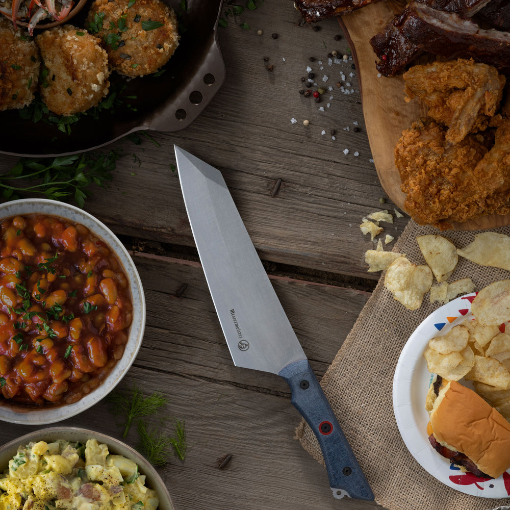 Assorted food items including fried chicken, fries, and a Messermeister Overland Chef Field and Flame Camp knife on a wooden surface.