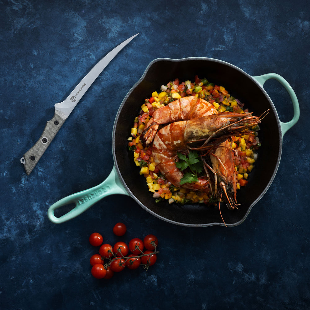 Skillet with prawns and vegetables on a dark blue background with Messermeister Overland Chef Fillet Knife