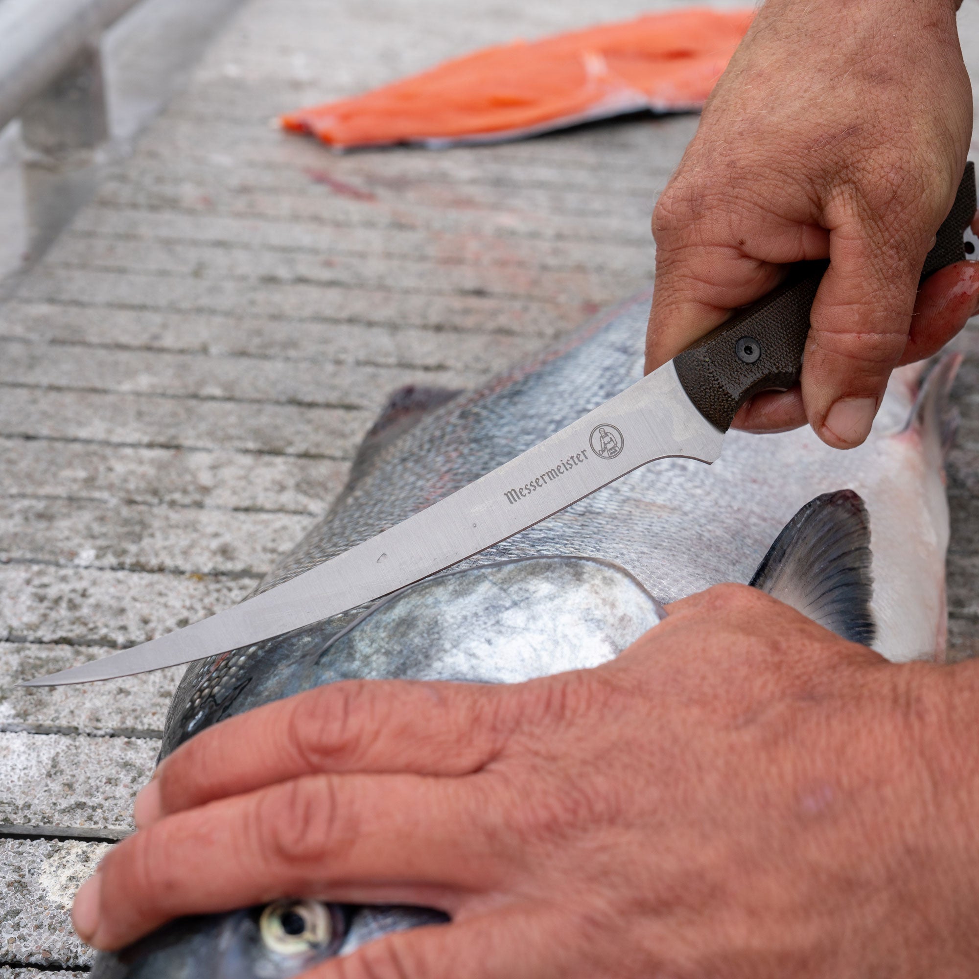 Person filleting a fish with a Messermeister Overland Chef Fillet knife on a wooden surface
