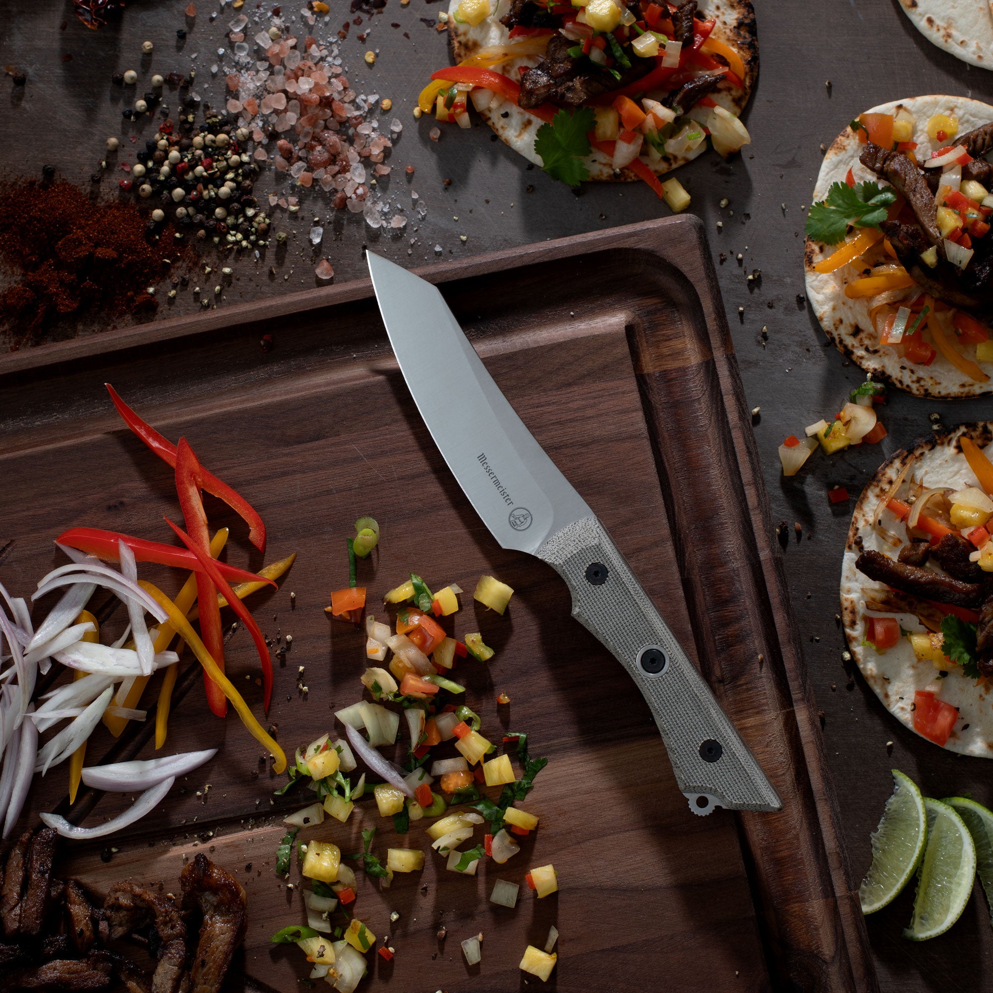 Messermeister Overland Chef Utility Knife on a wooden cutting board with chopped vegetables and tortilla pizzas.