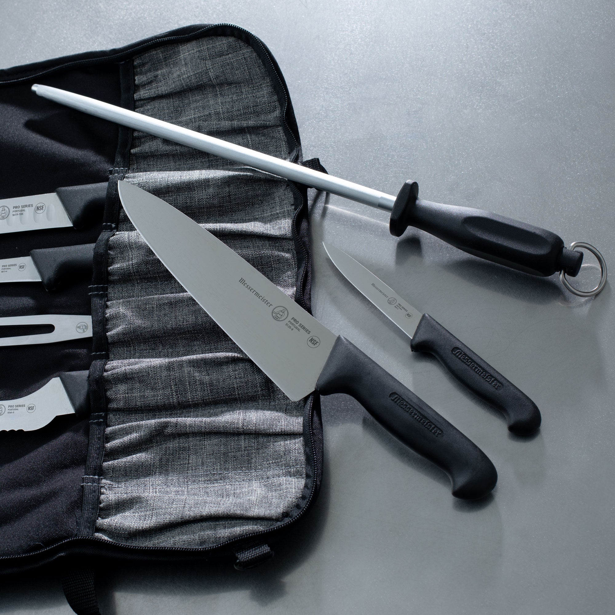 Messermeister Pro Series Chef and Paring Knife on a Messermeister Preservation Knife Luggage and a Messermeister Sharpening Steel on a Stainless Steel Prep Kitchen Counter