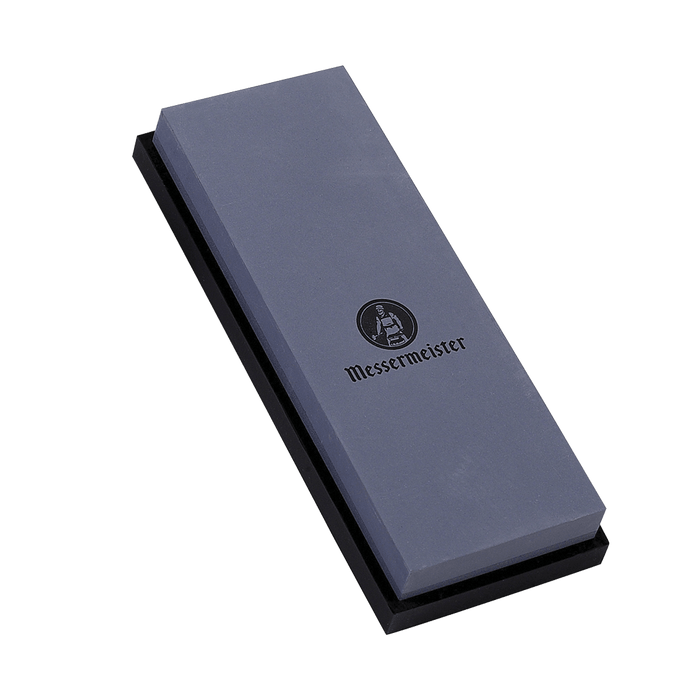 Messermeister 400 & 1000 grit Restoration Stone is a dual sided rectangle 8 inch x 3 inch x 1 inch. The top layer is gray with black "Messermeister" logo.  Bottom layer is black. The item sits in a rectangular black silicone base. Image tilted up and to the left.