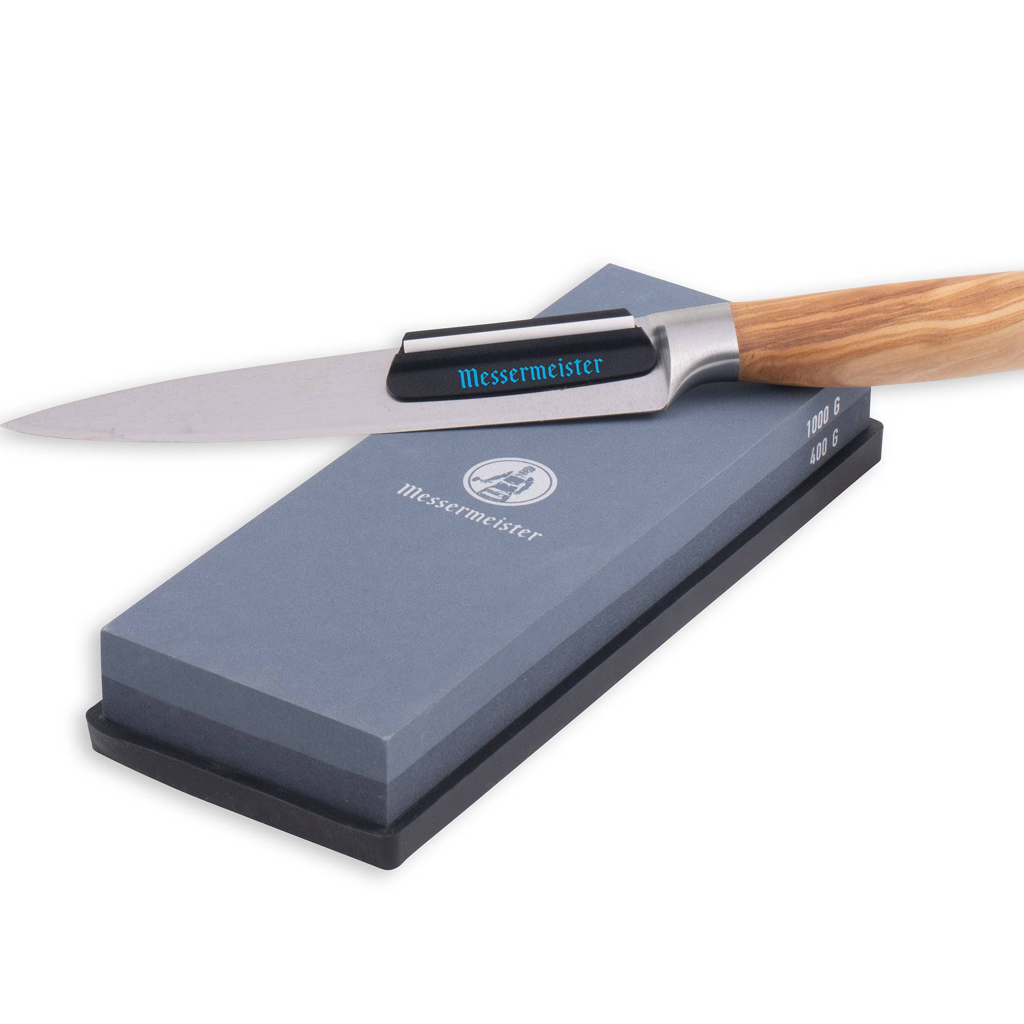 Messermeister 400 & 1000 grit Restoration Stone. The top layer is gray with silver "Messermeister" logo.  Bottom layer is black. The item sits in a rectangular black silicone base. A wooden knife with angle guide is resting along the top of the stone.