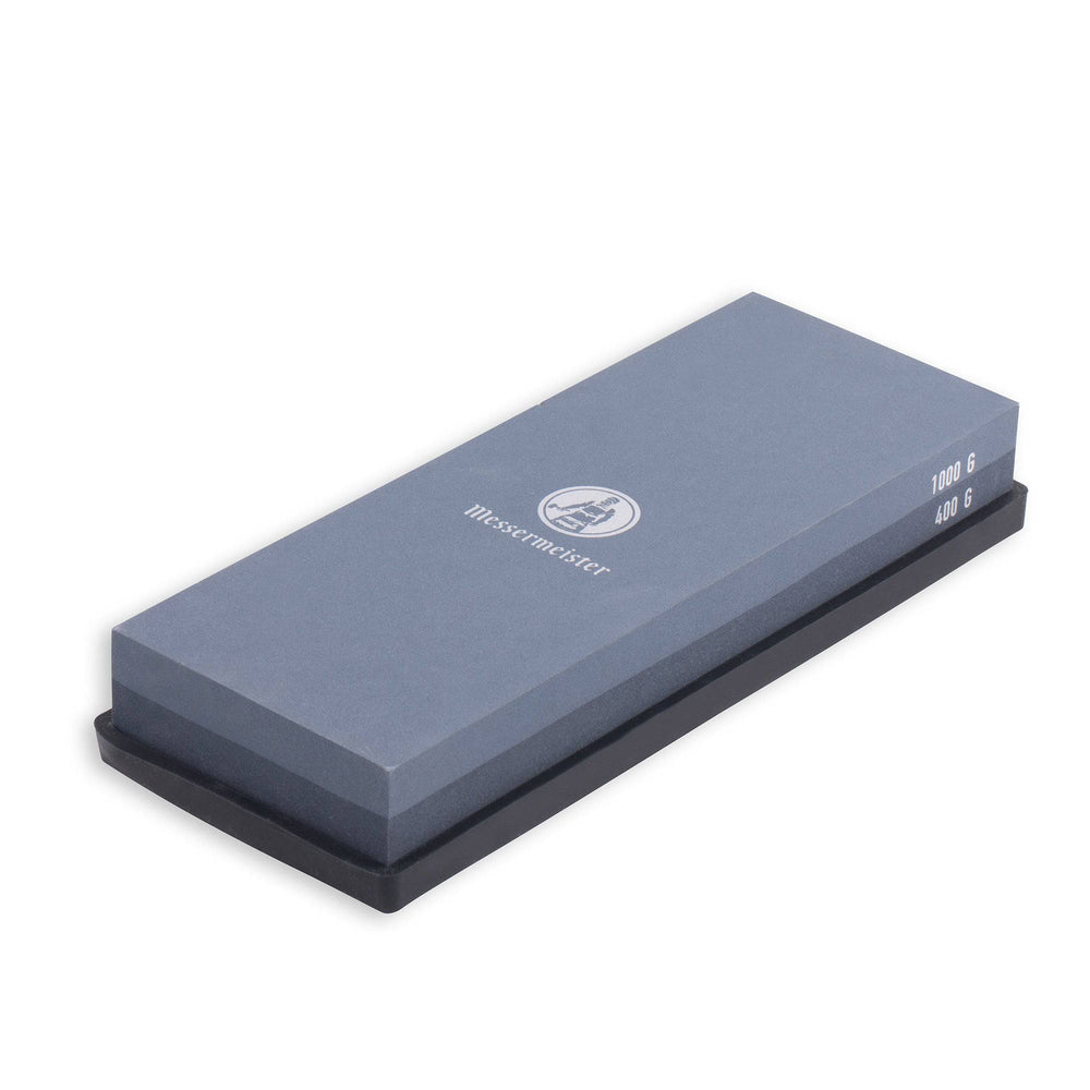 Messermeister 400 & 1000 grit Restoration Stone is a dual sided rectangle 8 inch x 3 inch x 1 inch. The top layer is gray with silver "Messermeister" logo.  Bottom layer is black. The item sits in a rectangular black silicone base. Image tilted slightly up and to the right on a white background.