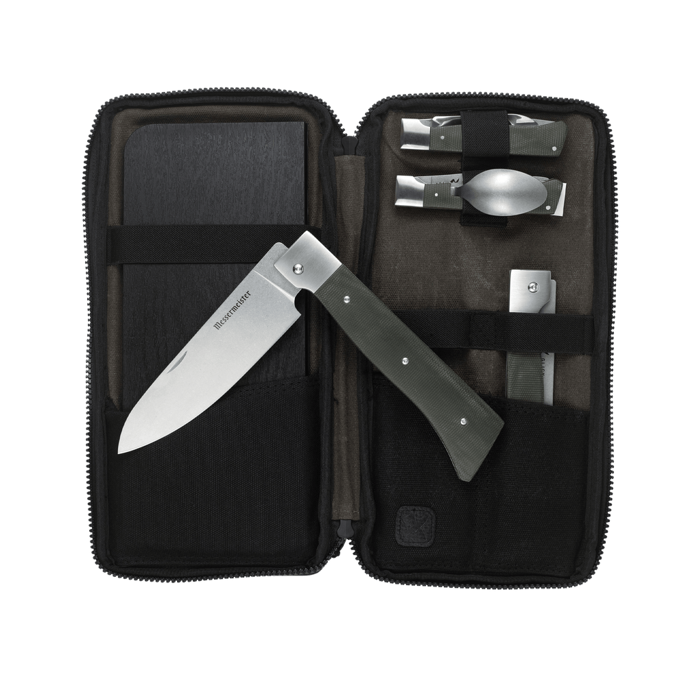 Messermeister Adventure Chef Linen Summit 6 Piece set showing the 6 inch folding Chef's Knife removed and laying on top of the open zippered carrying case with the folding utensil, folding peeler and parer, folding fillet knife and faux wood cutting board tucked inside.