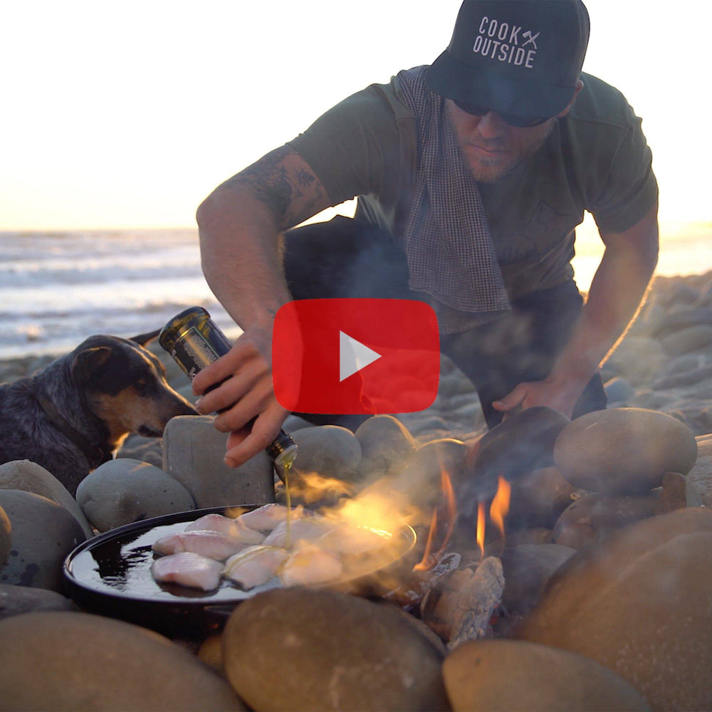 Video of cooking fish on the beach at sunset over a firepit made of rocks and driftwood 