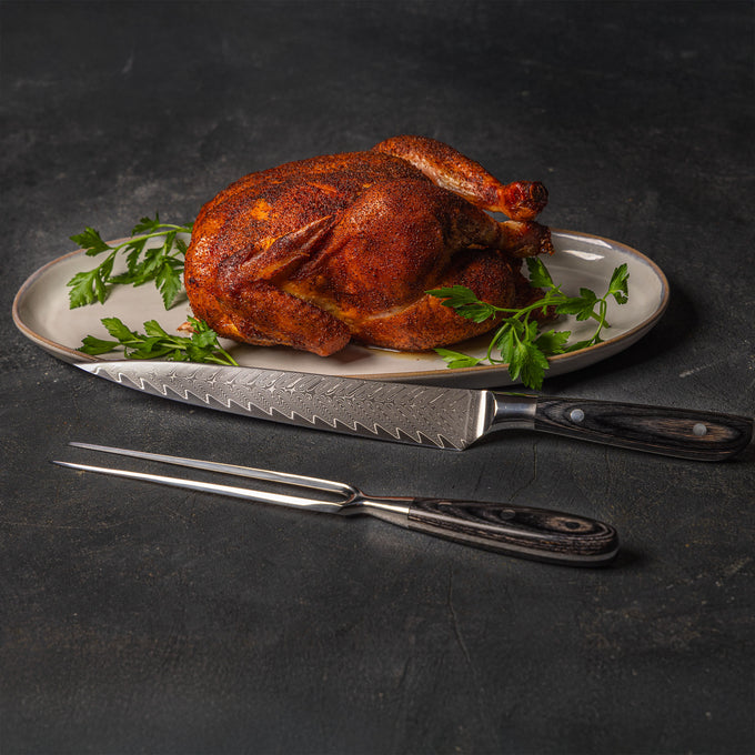 Messermeister Avanta Damascus carving knife and fork set with roasted chicken  on styled plate on black table