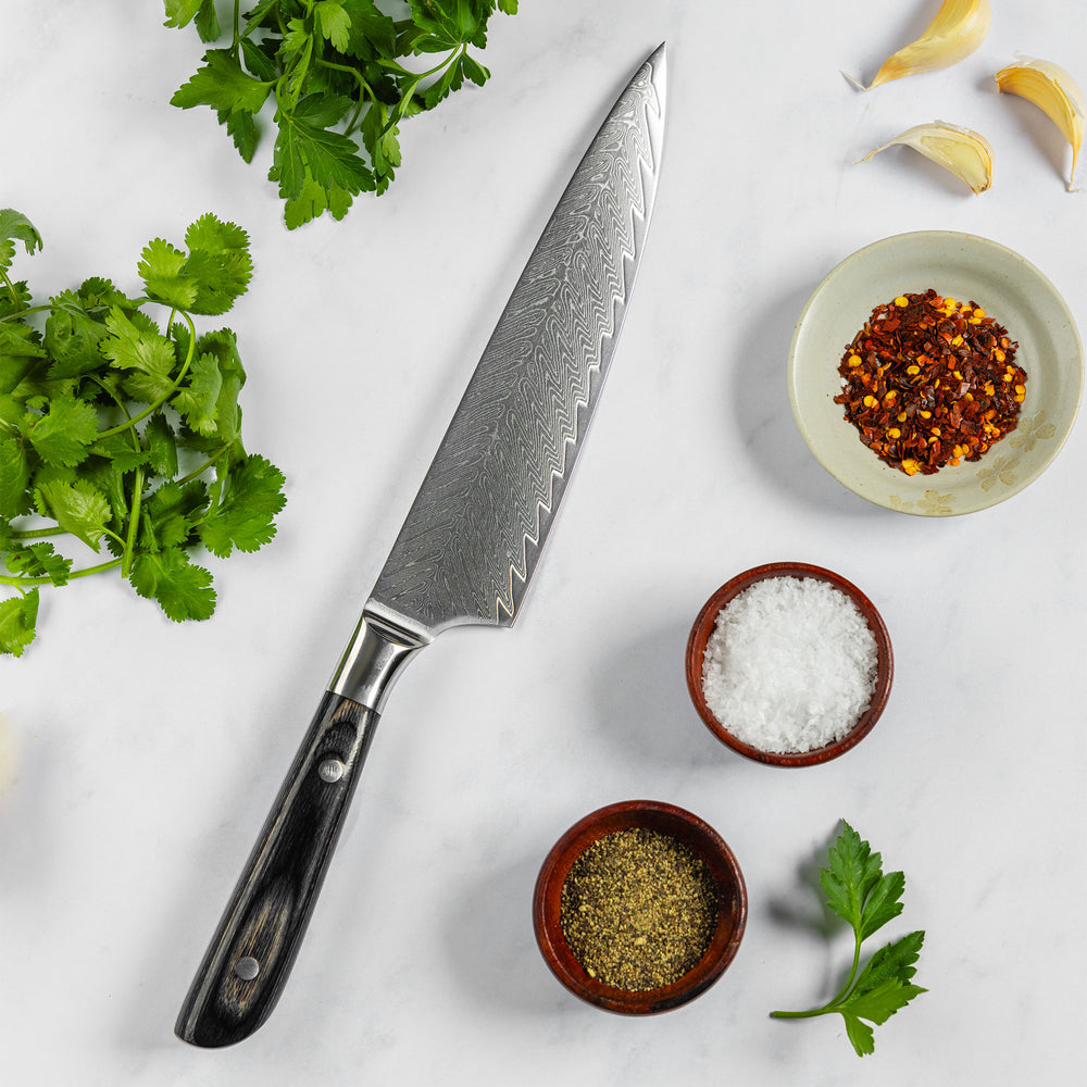 Messermeister Avanta Damascus chef knife with ebony pakkawood handle on white surface with herbs and spices