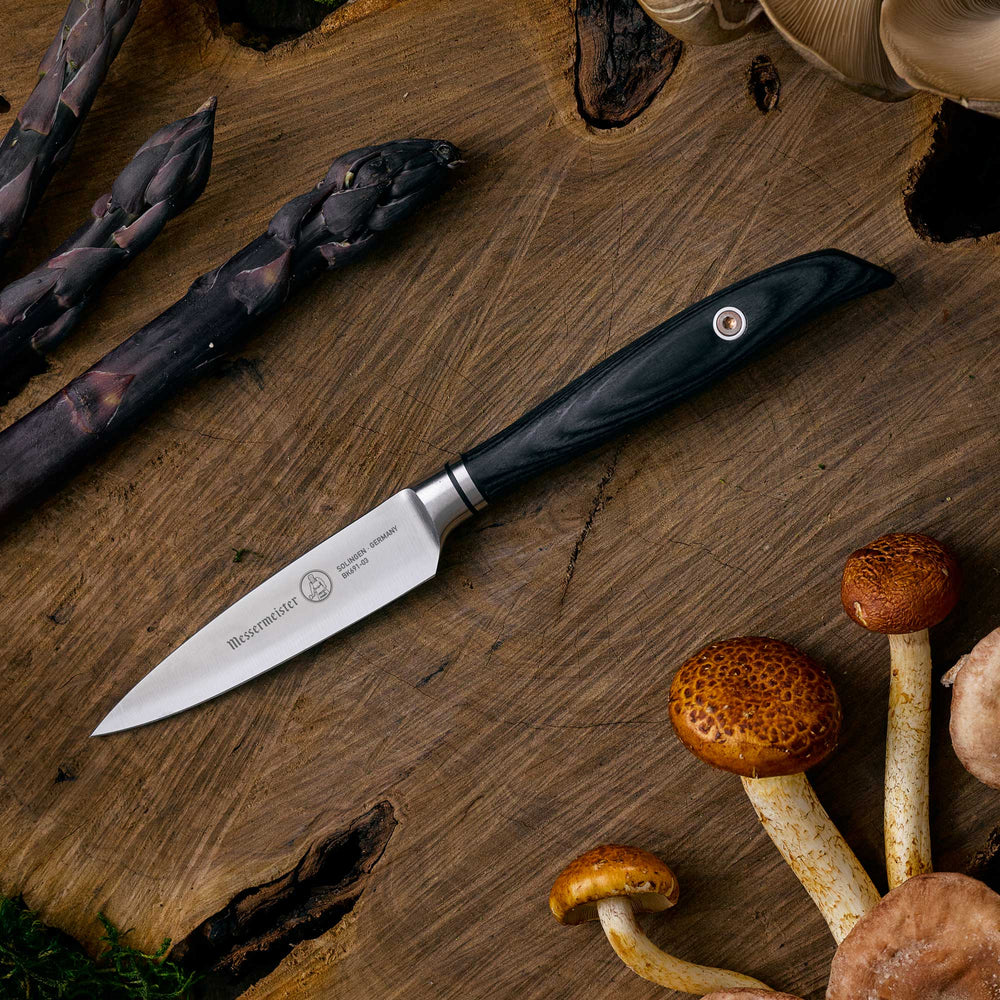 Messermeister Blacksmith Paring Knife - 3.5" with stainless steel blade and ebony pakkawood handle" - on a wooden cutting board with mushrooms and asparagus