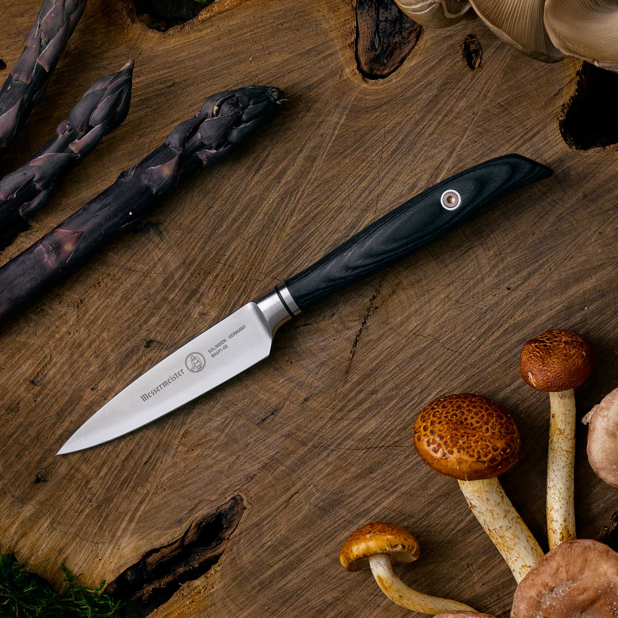 Messermeister Blacksmith Paring Knife - 3.5" with stainless steel blade and ebony pakkawood handle" - on a wooden cutting board with mushrooms and asparagus