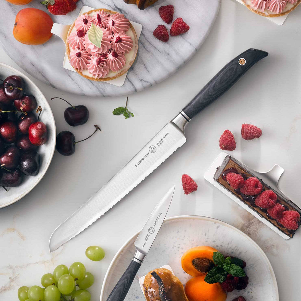Messermeister Blacksmith Scalloped Slicing Knife 8.5 inch with stainless steel blade and ebony pakkawood handle on a table surrounded by varied berries and fruits