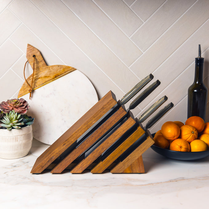 Messermeister Carbon 5 Piece Next Level Block Set shown with knives resting inside of knife block on a counter with oranges and succulents in the background